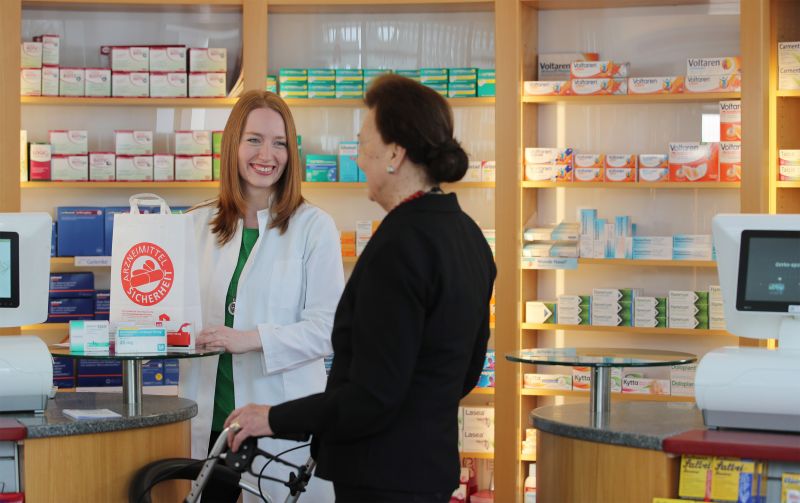 Post "Medikationsanalyse, Impfberatung, Diabetesprävention - unsere Leistung für dich". Eine Apothekerin hat Medikamente für ihre Kundin bereitgestellt.